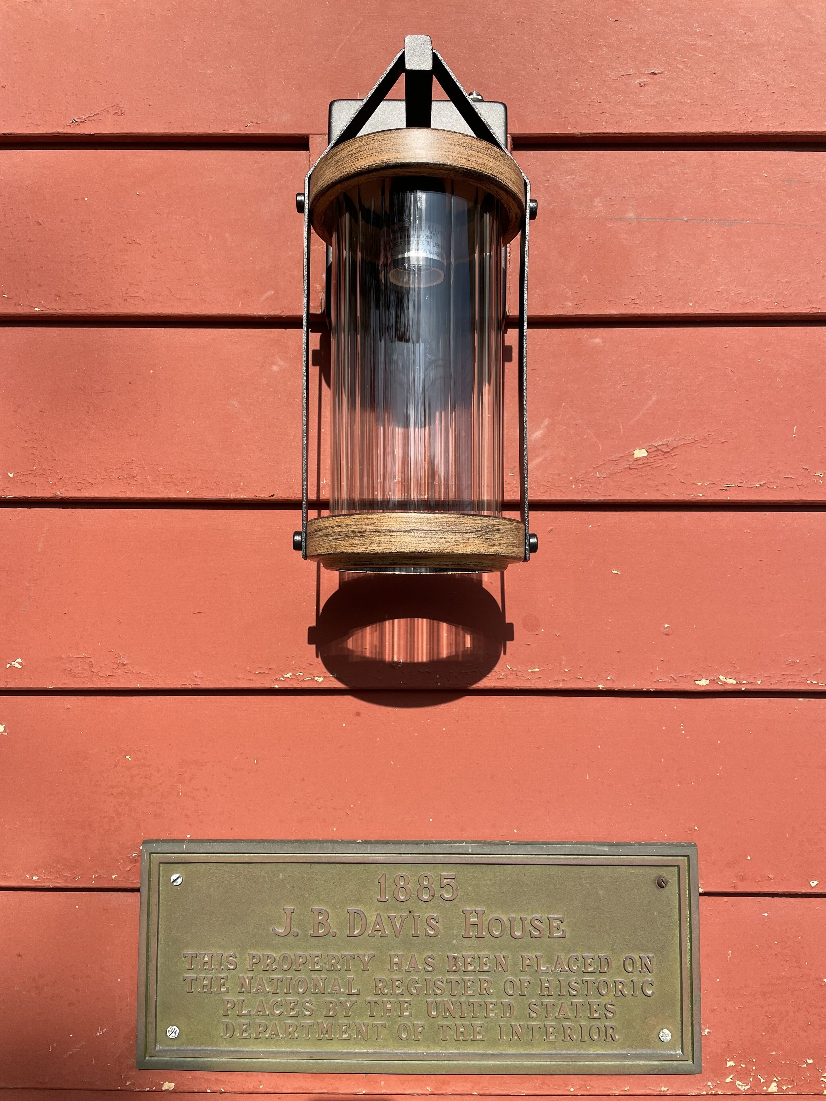 Una placa de latón en una pared de madera roja con la inscripción 'Casa J.B. Davis 1885, esta propiedad ha sido incluida en el Registro Nacional de Lugares Históricos por el Departamento del Interior de los Estados Unidos'.