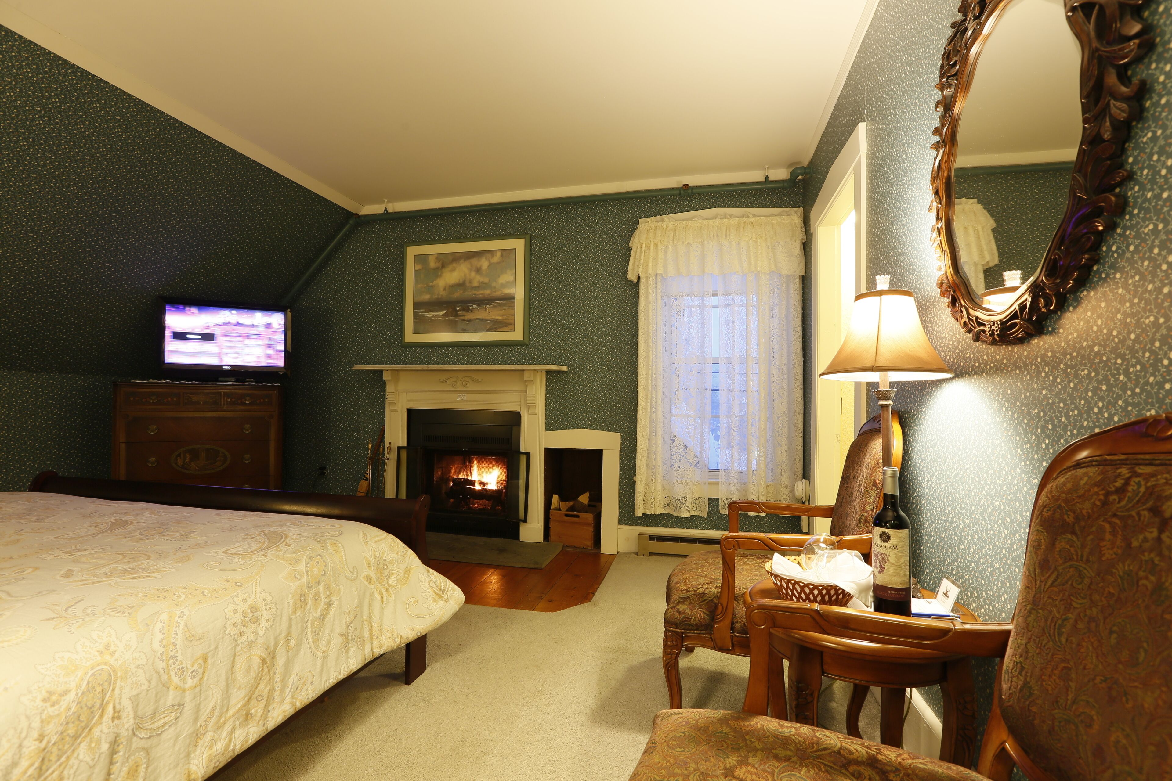 A hotel room with a bed, a fireplace, a television, and a dining area with a table and chairs.
