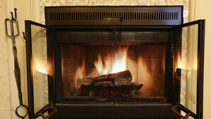 Una chimenea con fuego encendido en su interior, una reja metálica y un tirador en el lado derecho.