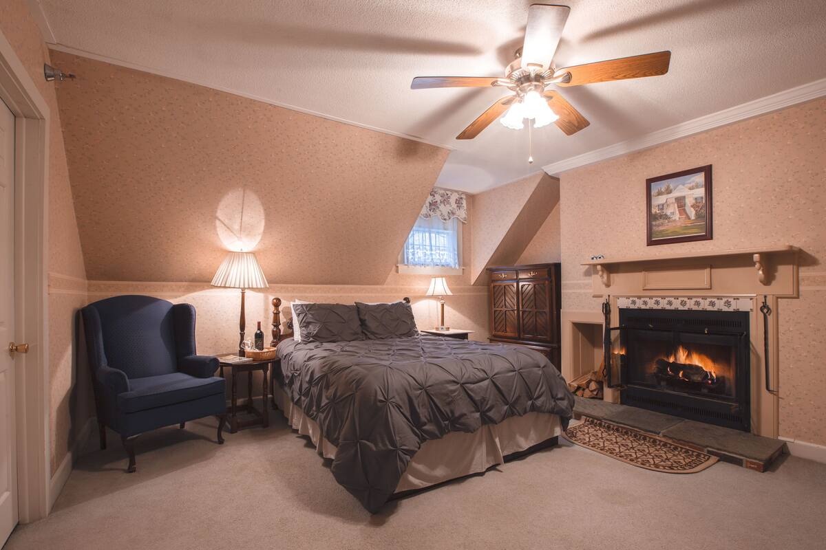 A bedroom with a bed, a chair, a fireplace, and a ceiling fan.
