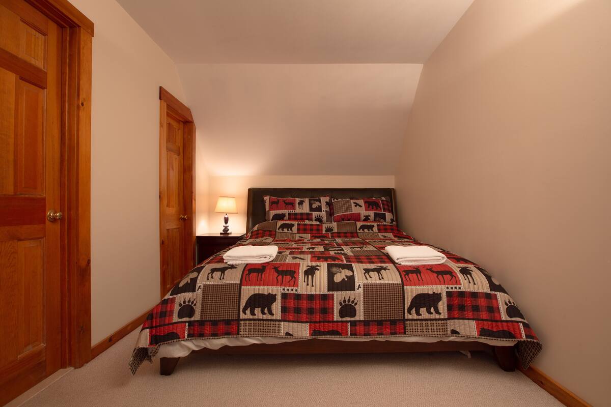 A bedroom with a bed, wooden doors, a nightstand with a lamp, and a quilt with animal patterns.