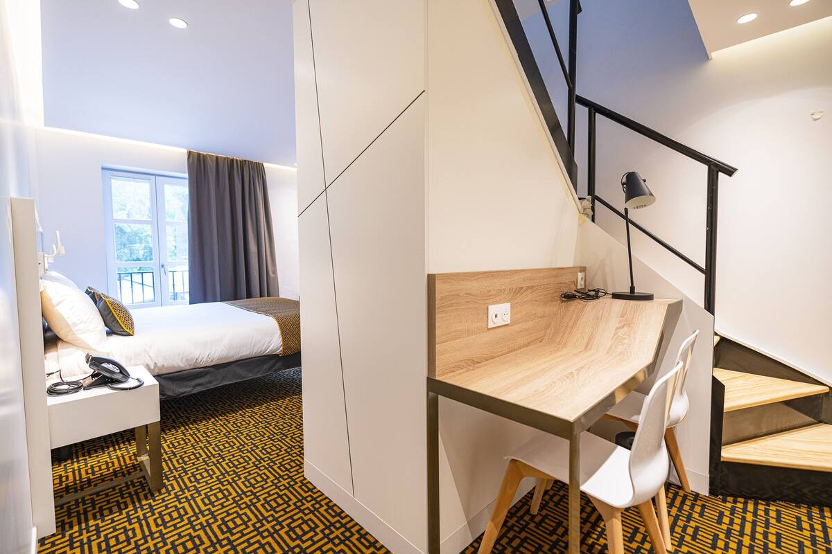 Een hotelkamer met een bed, een bureau, een stoel, een trap en een vloer met een patroon.