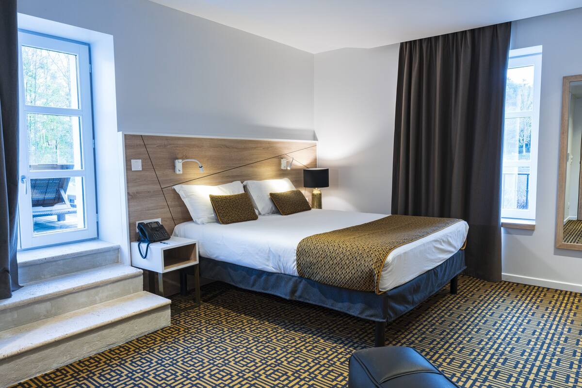 Een moderne hotelkamer met een groot bed, een nachtkastje met een lamp, een telefoon en een raam met gordijnen.