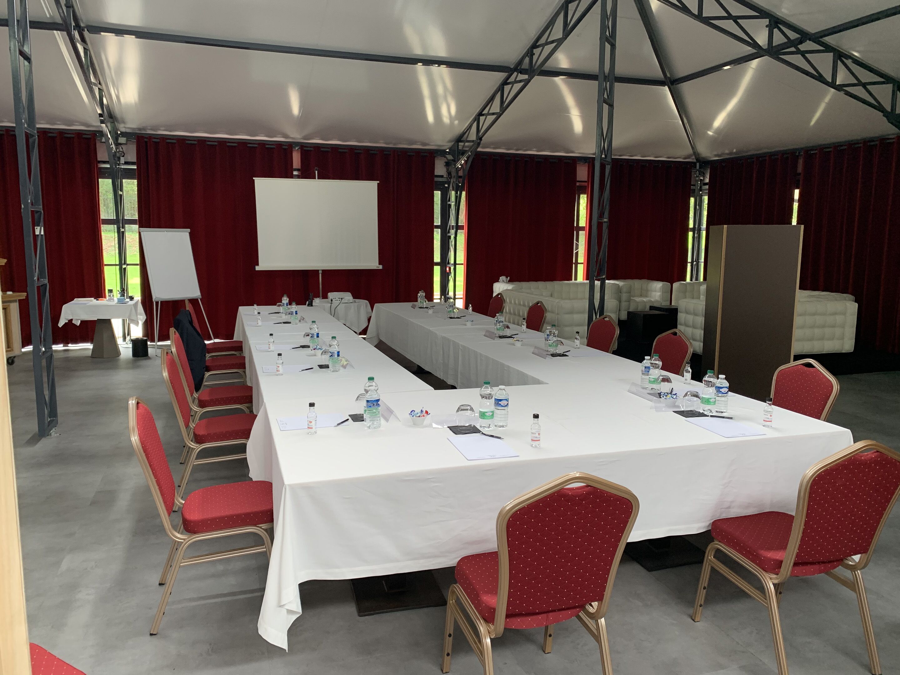 Un salón de conferencias con una larga mesa, sillas rojas, manteles blancos y una pizarra.