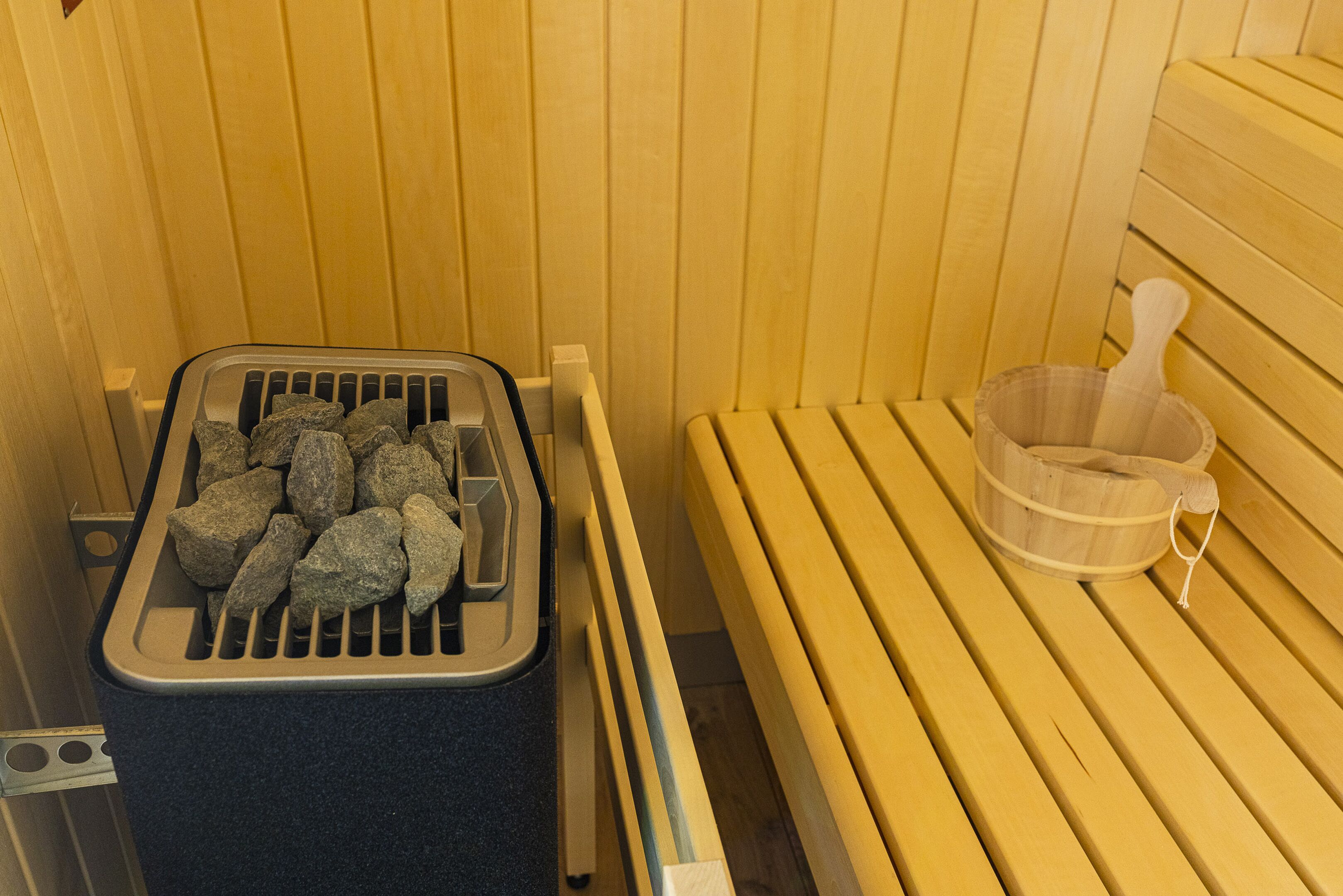 A sauna with wooden benches, a stone heating tray, and a wooden bucket.