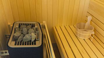 A sauna with wooden benches, a stone heating tray, and a wooden bucket.