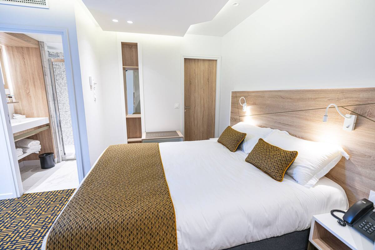 Een moderne hotelkamer met een groot bed, telefoon op het nachtkastje en een houten hoofdeinde.