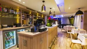 A bar area with a counter, shelves with bottles, and a refrigerator. There are tables and chairs in the dining area.