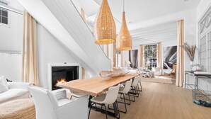 A modern living room with a long wooden table, white sofas, and a fireplace.