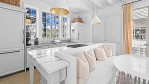 A modern kitchen with white cabinetry, a central island with seating, pendant lighting, and a view of the outdoors.