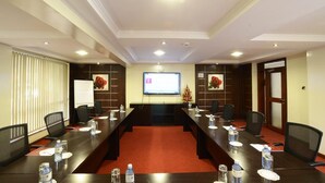 A conference room with a long table, chairs, a projector screen, and a whiteboard. - Travellers Safari - Waridi (Nairobi)