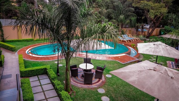 A circular swimming pool with a surrounding patio area, including a table and chairs, and a covered seating area. - Travellers Safari - Waridi (Nairobi)