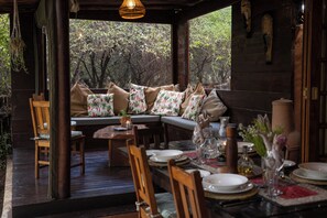 A cozy outdoor dining area with wooden furniture, a cushioned bench, and a view of lush greenery. - Braai Safaris Lodge (Hoedspruit)
