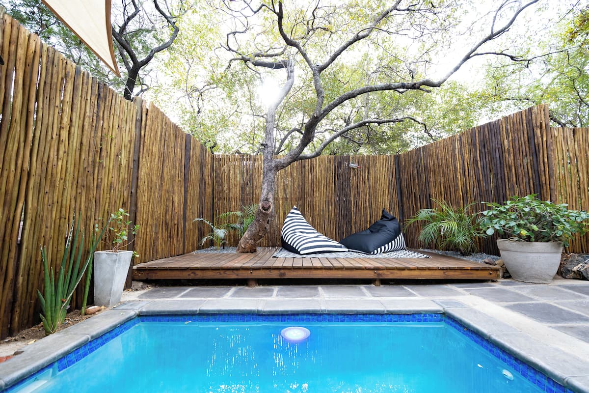 A backyard with a swimming pool, wooden deck, and a tree.
