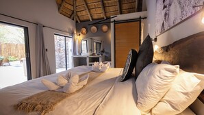A well-lit bedroom with a bed, a large window, and a thatched ceiling. - Braai Safaris Lodge (Hoedspruit)