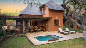 A house with a thatched roof, a pool, and outdoor seating. - Braai Safaris Lodge (Hoedspruit)