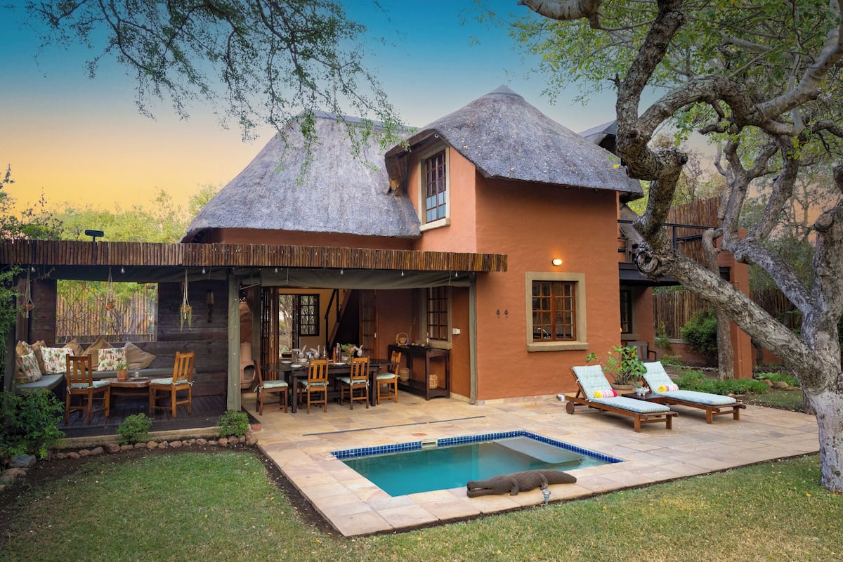 A house with a thatched roof, a pool, and outdoor seating.