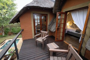 A thatched-roof room with a bed, a small table, and a chair. - Braai Safaris Lodge (Hoedspruit)