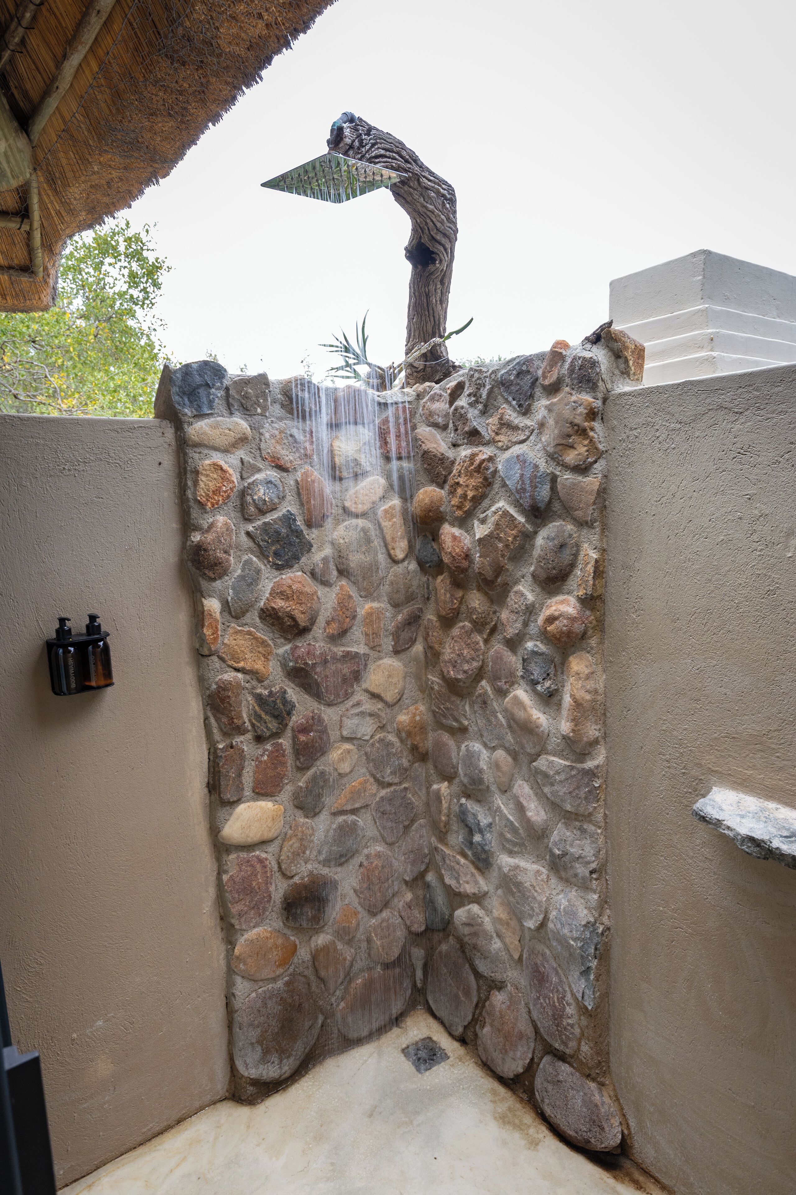 A stone shower enclosure with a waterfall feature, a thatched roof, and a stone wall.
