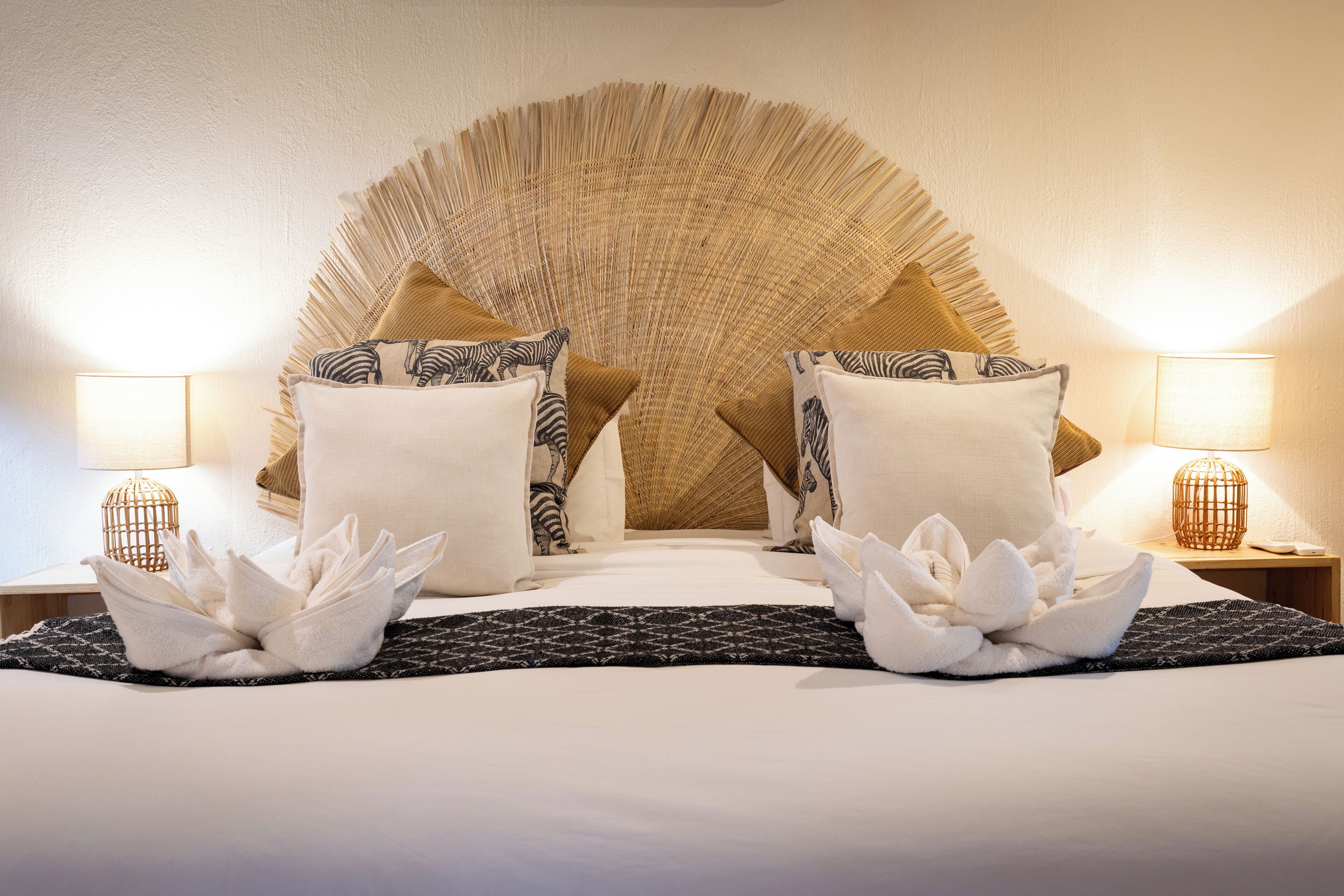 A neatly made bed with white linens, two decorative pillows, and a large, textured wall arch behind it.