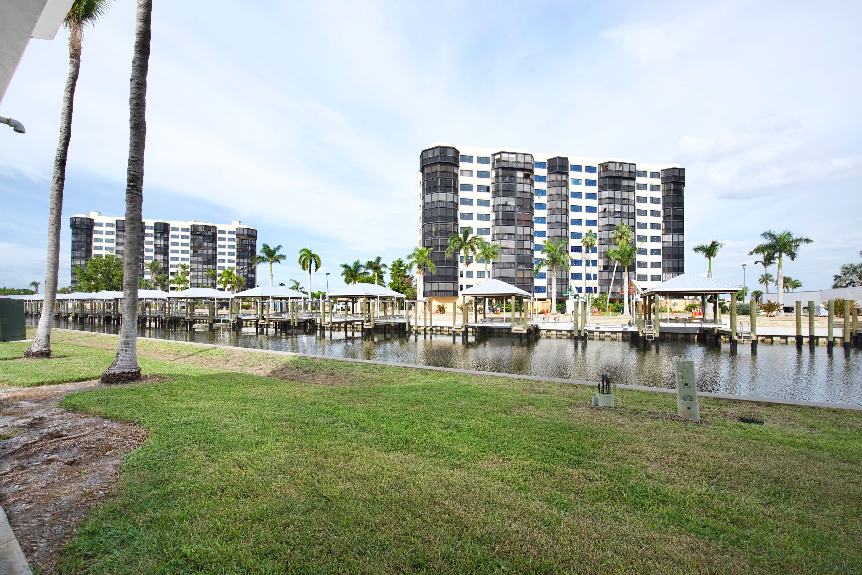 A waterfront hotel with multiple high-rise buildings, a dock area with covered structures, and a grassy foreground.