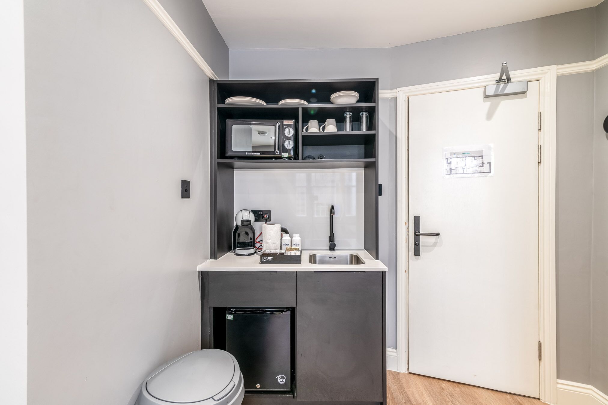 Una kitchenette compacta equipada con microondas, cafetera y lavabo.