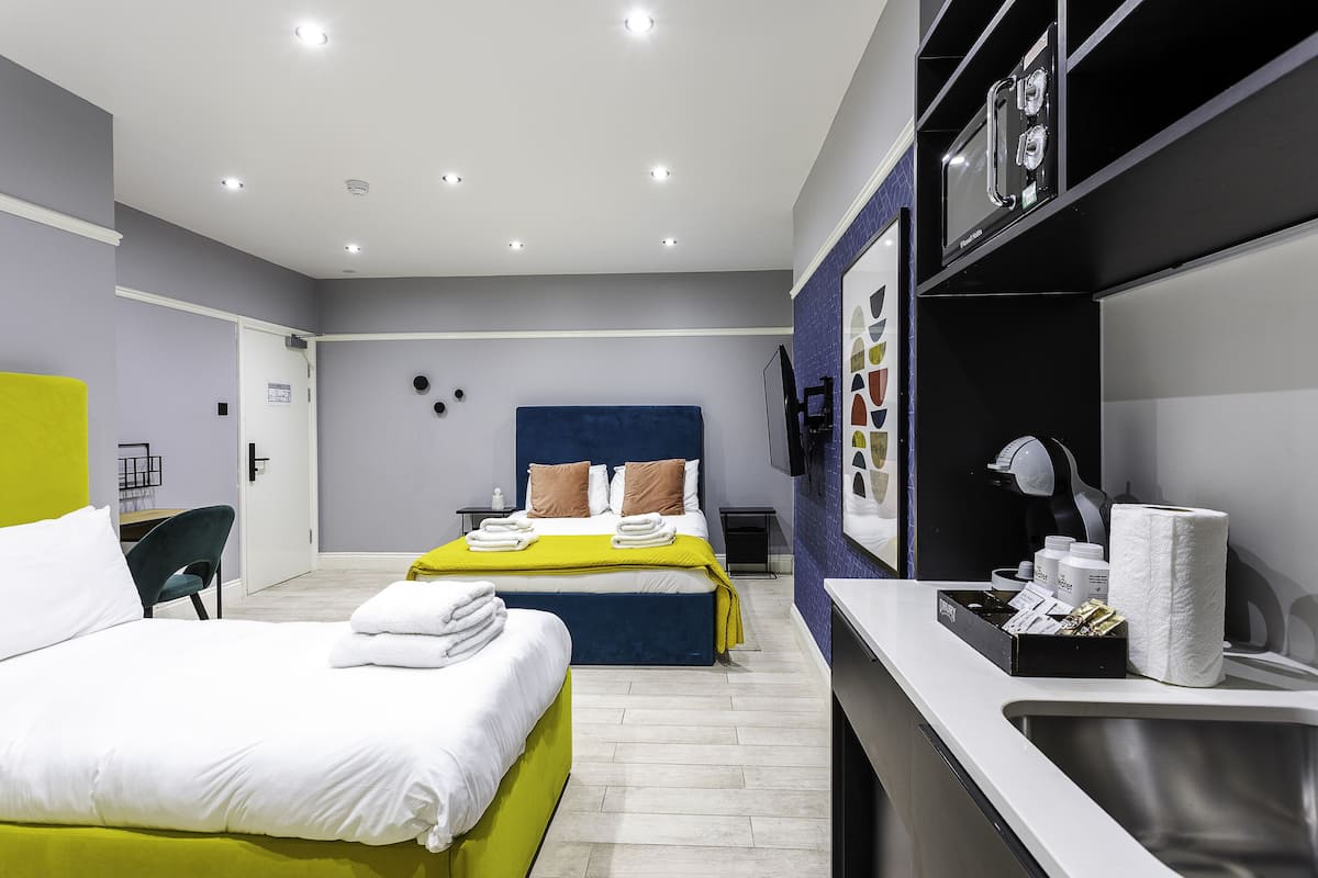 A modern hotel room with a large bed, a smaller bed, a desk, and a bathroom.