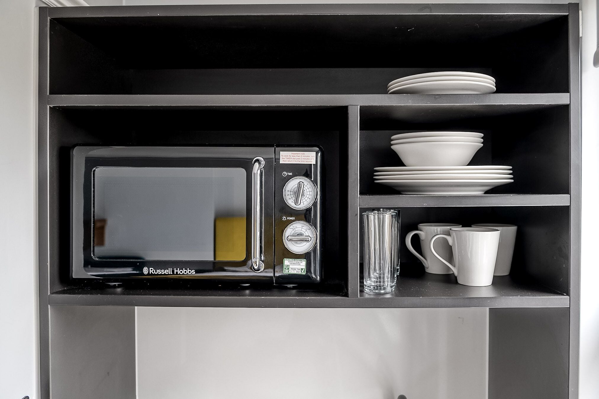 A kitchen with a built-in microwave, a glass, and stacked white dishes.