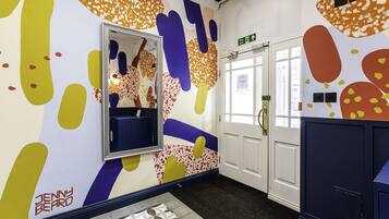 A hallway with a mirror, a door with an exit sign, and a patterned floor.