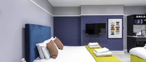 A modern hotel room with a large bed, a TV mounted on the wall, and a small kitchenette.