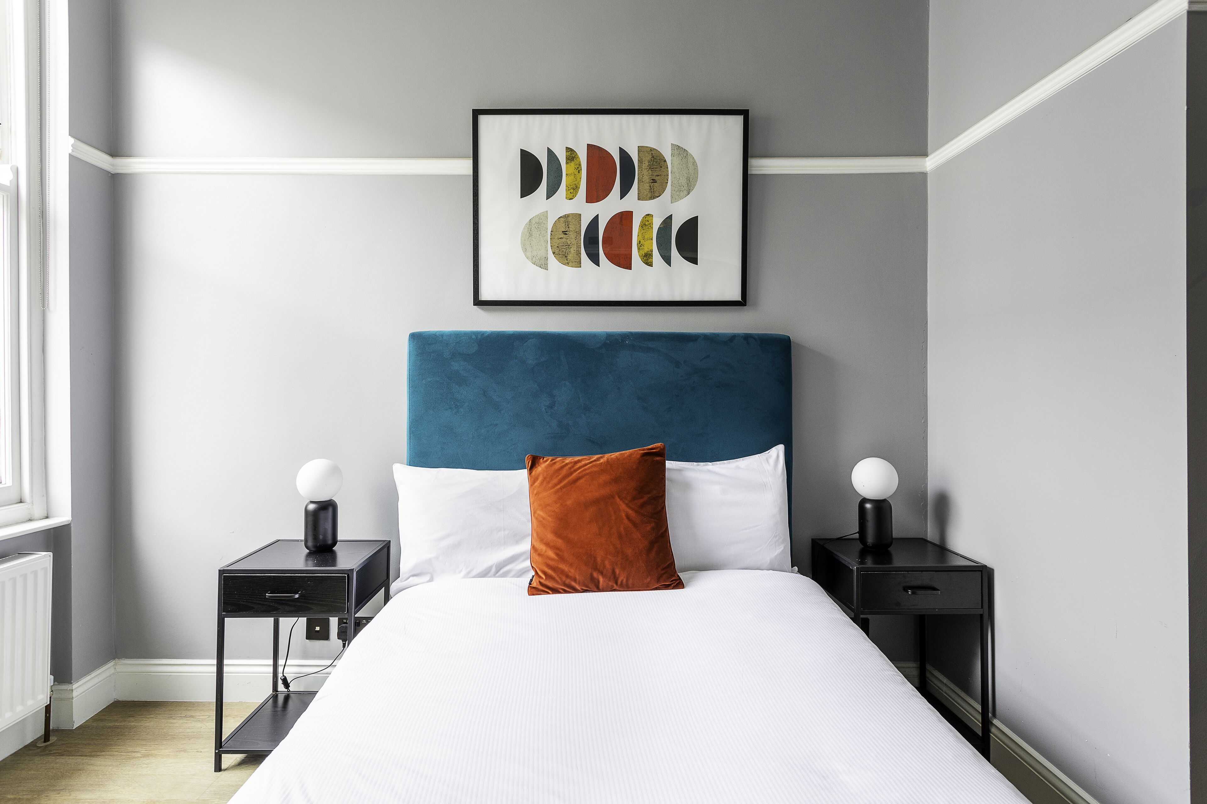 A bedroom with a bed, two bedside tables, a framed artwork, and a window.