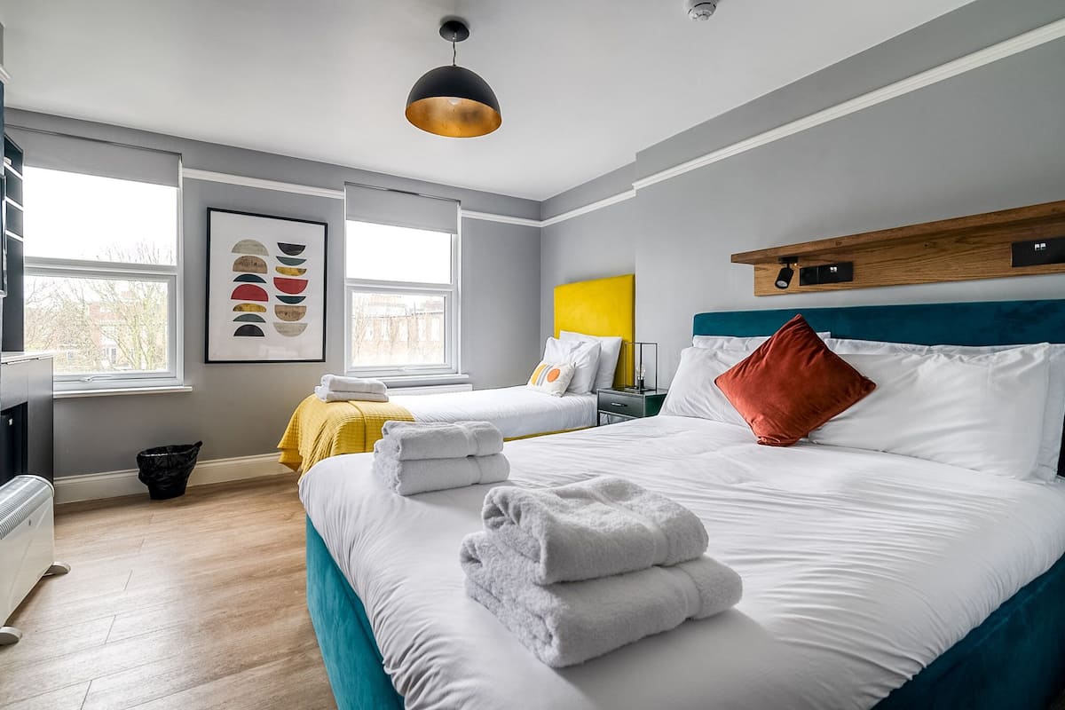 A hotel room with two beds, a large window, a modern pendant light, and a framed artwork on the wall.