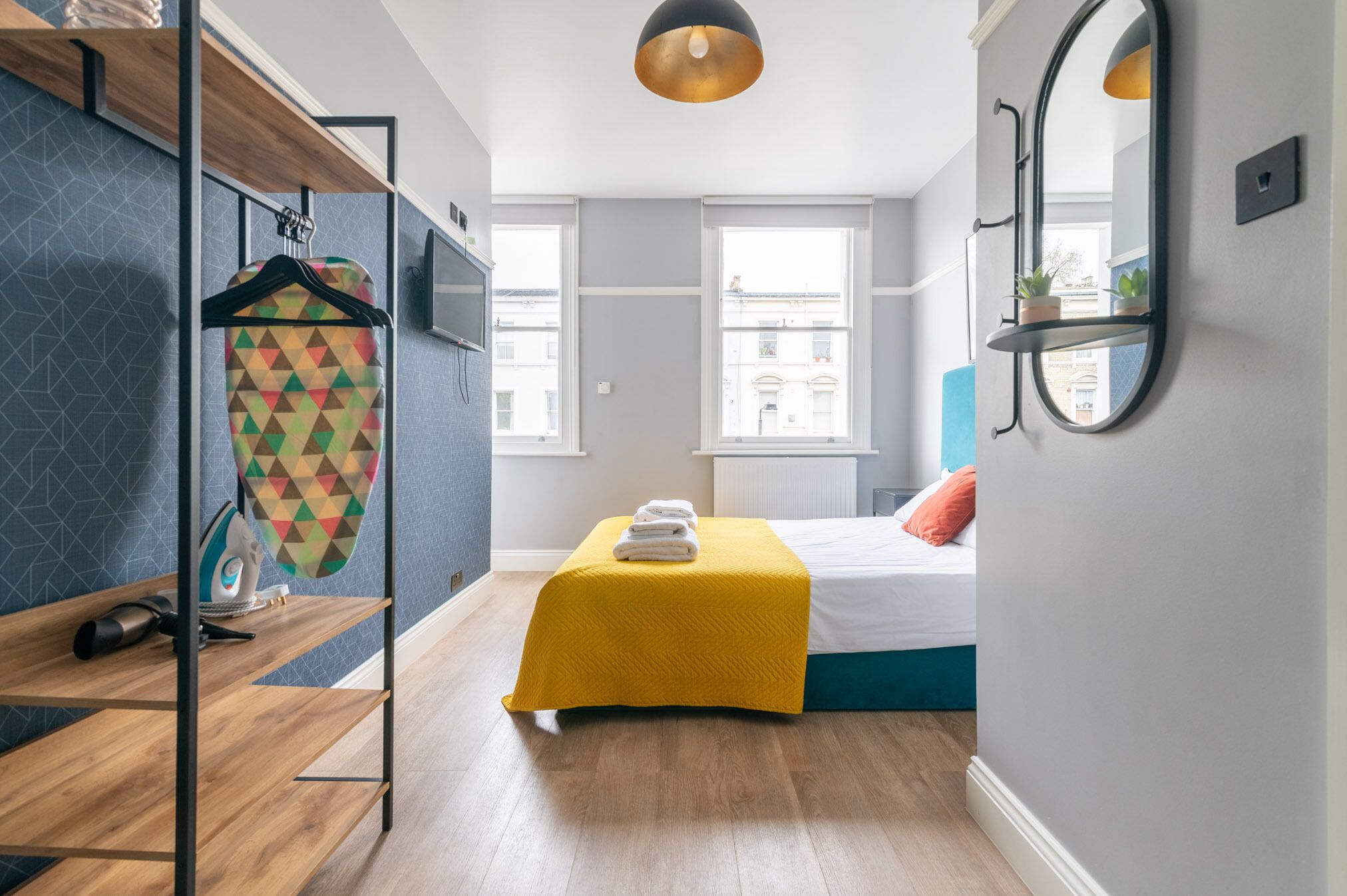 Un dormitorio moderno con una cama, una colcha amarilla, un tendedero y un espejo en la pared.