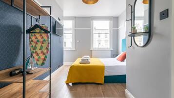 A modern bedroom with a bed, a yellow bedspread, a hanging laundry rack, and a mirror on the wall.