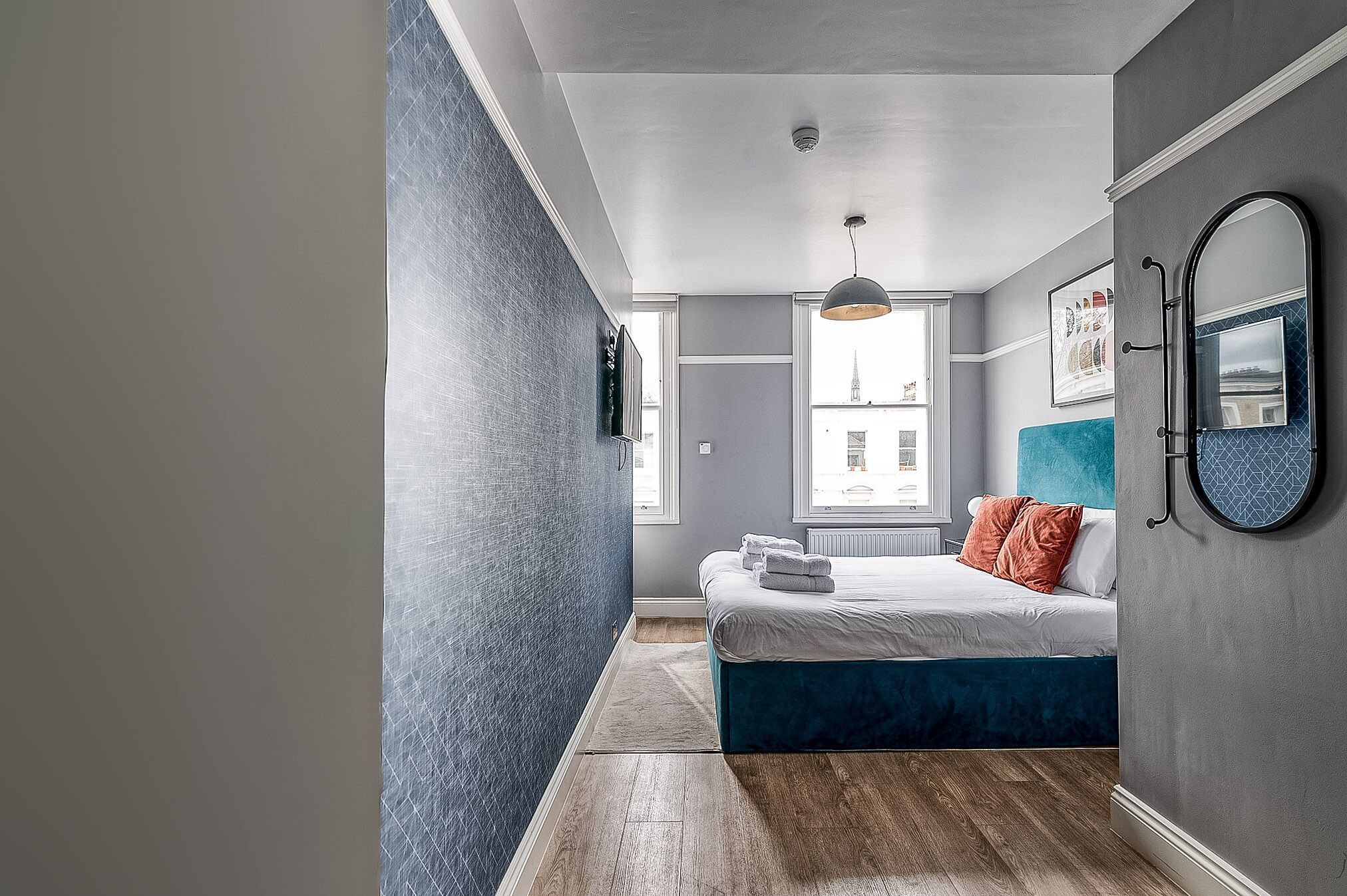 Un dormitorio moderno con una cama grande, una pared de acento azul y vistas de la ciudad a través de la ventana.