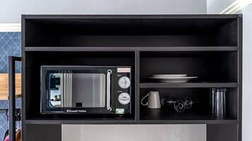 Eine kompakte Küche mit integriertem Mikrowellenherd, einem Regal mit Tellern und einer Tasse sowie einem kleinen Schrank.