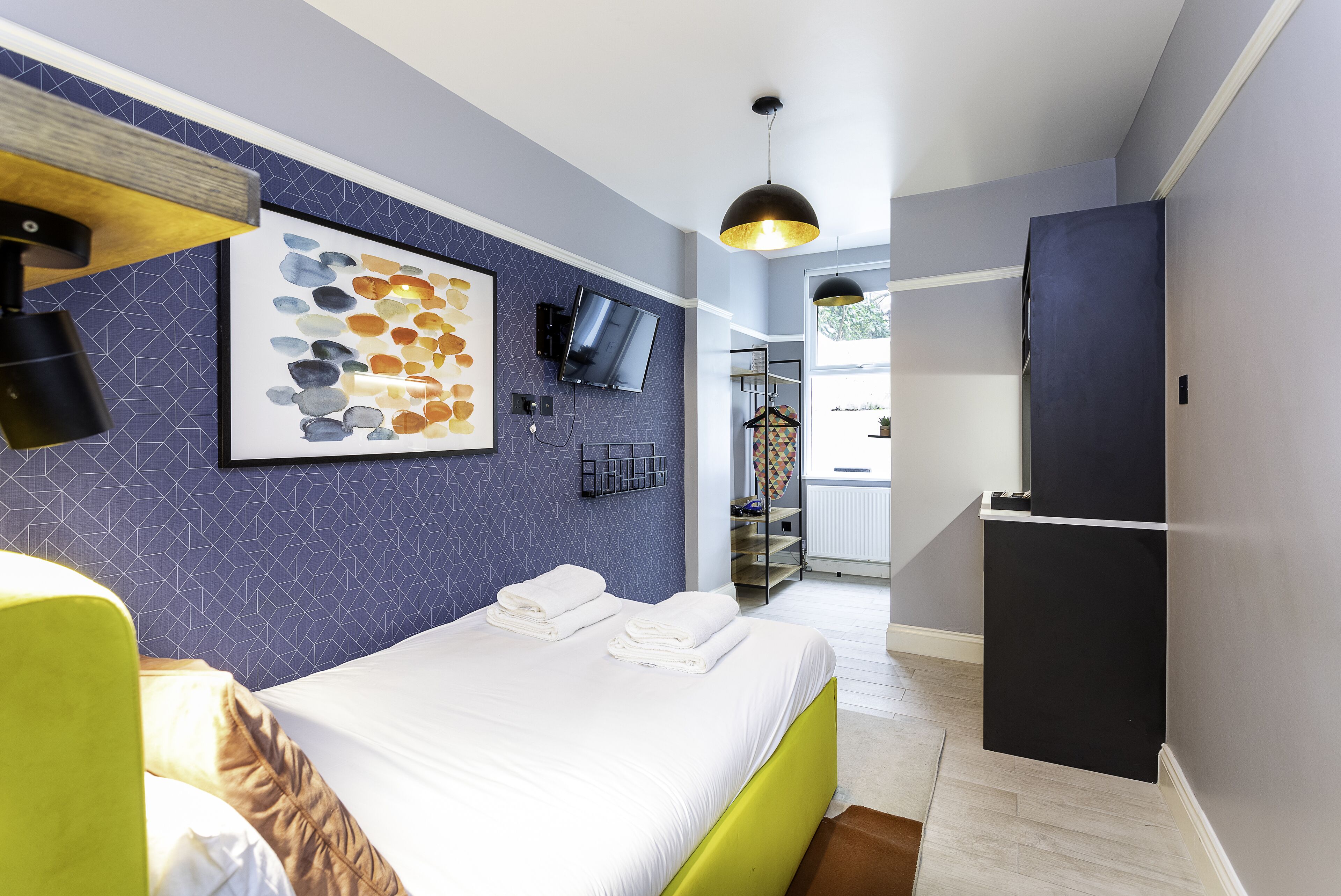 Una habitación de hotel moderna con cama, televisión, armario y baño visible a través de una puerta abierta.