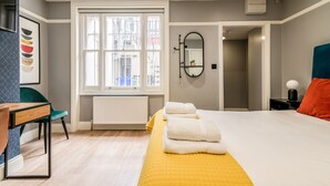 Un dormitorio moderno con una cama grande, una mesita de noche, una silla, una ventana con vistas y un espejo en la pared.