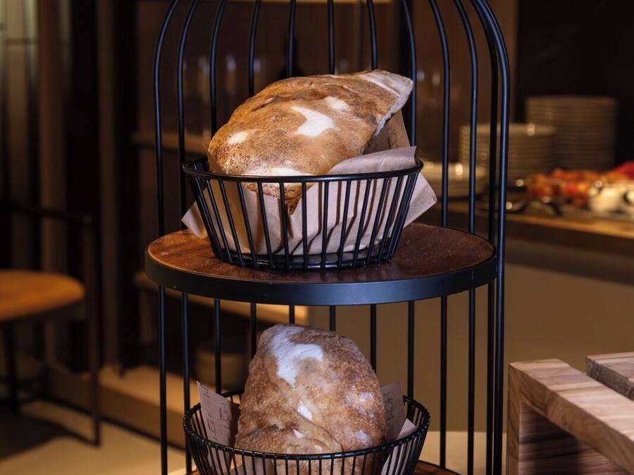 Un atril metálico de tres niveles con cestas para pan sobre una mesa redonda en un restaurante.