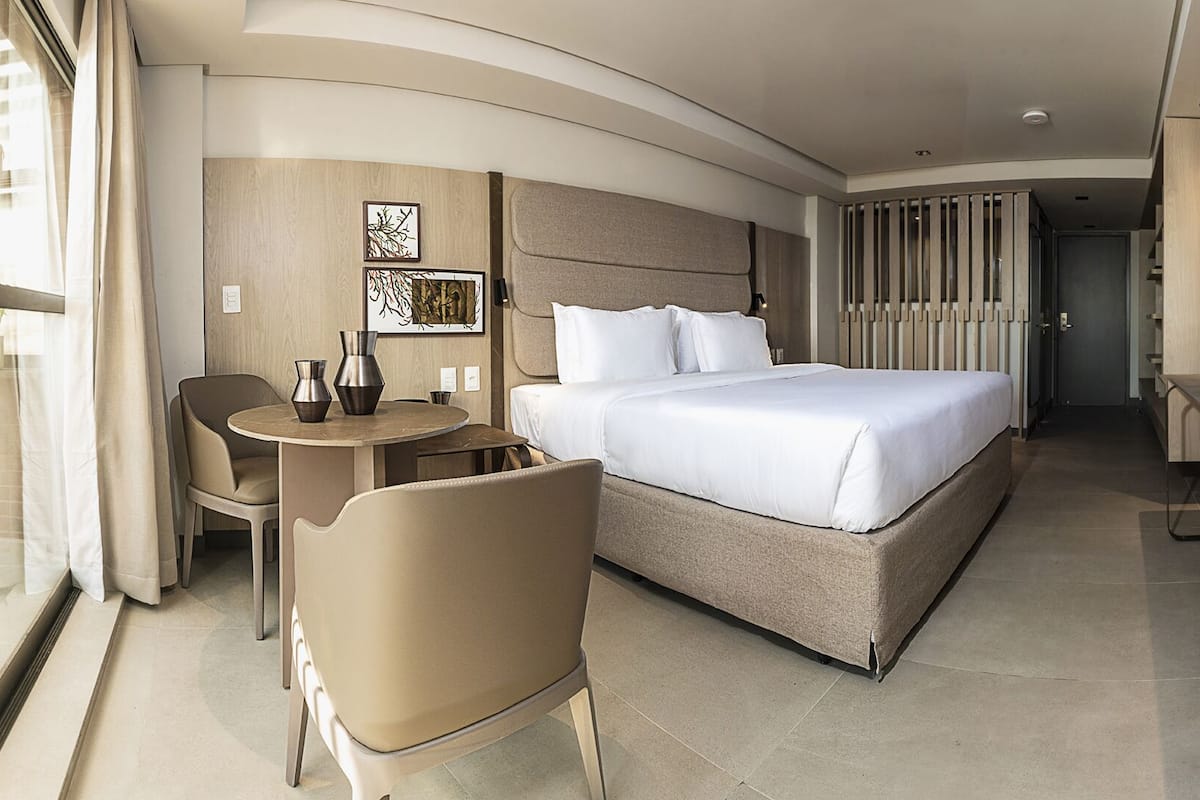 Una habitación de hotel moderna con una cama grande, un escritorio con sillas, un televisor y obras de arte en las paredes.