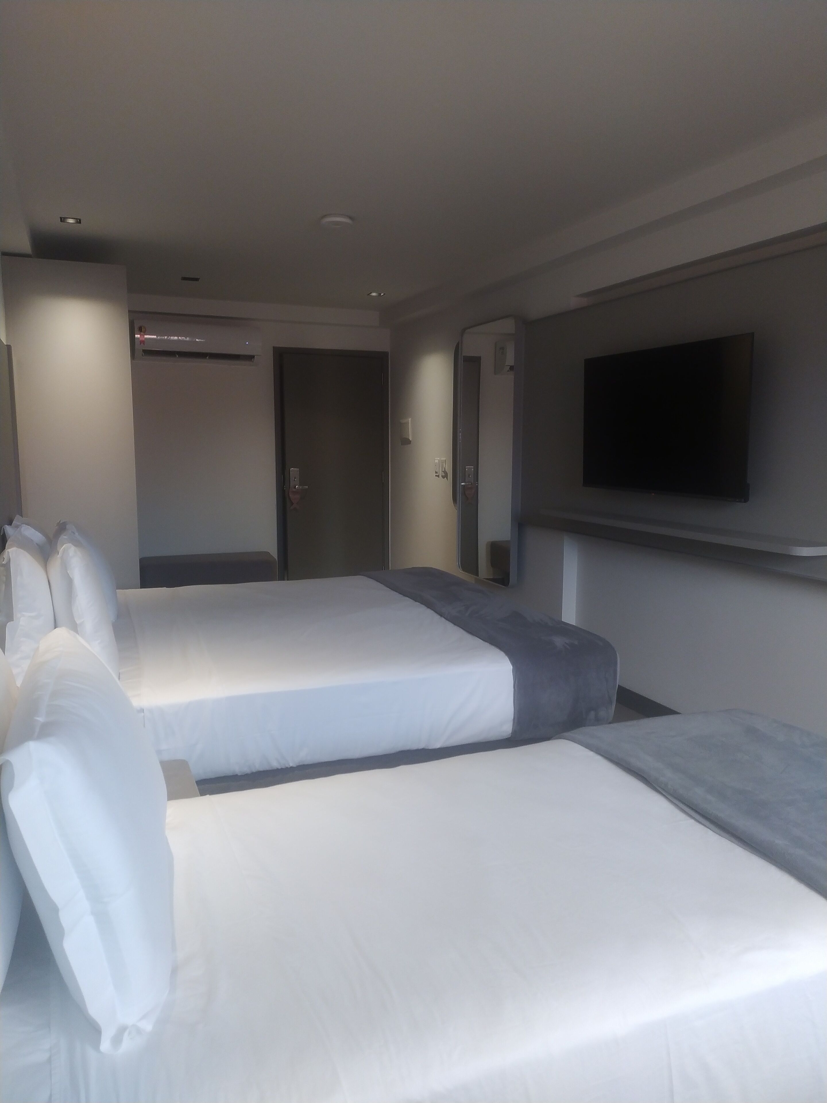 Quarto de hotel com duas camas, uma TV de tela plana na parede e um aparelho de ar condicionado.