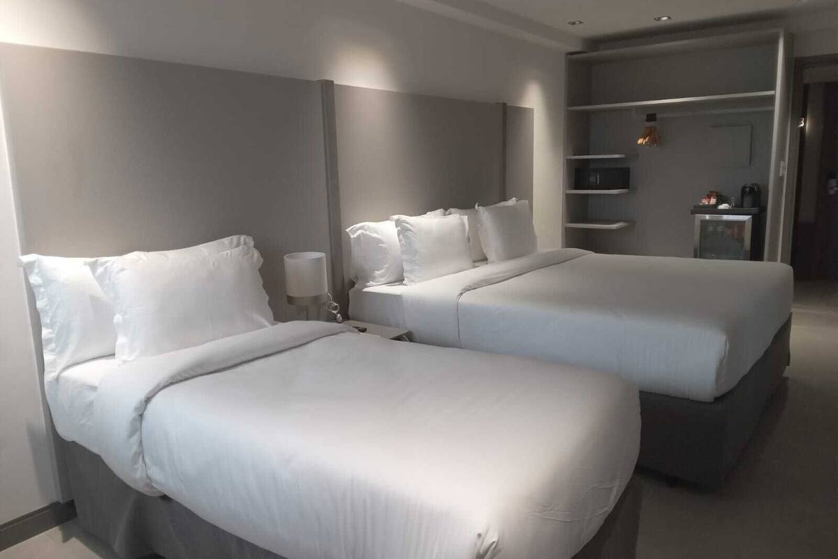 Habitación de hotel con dos camas, una mesita de noche con lámpara y un armario con estantes.