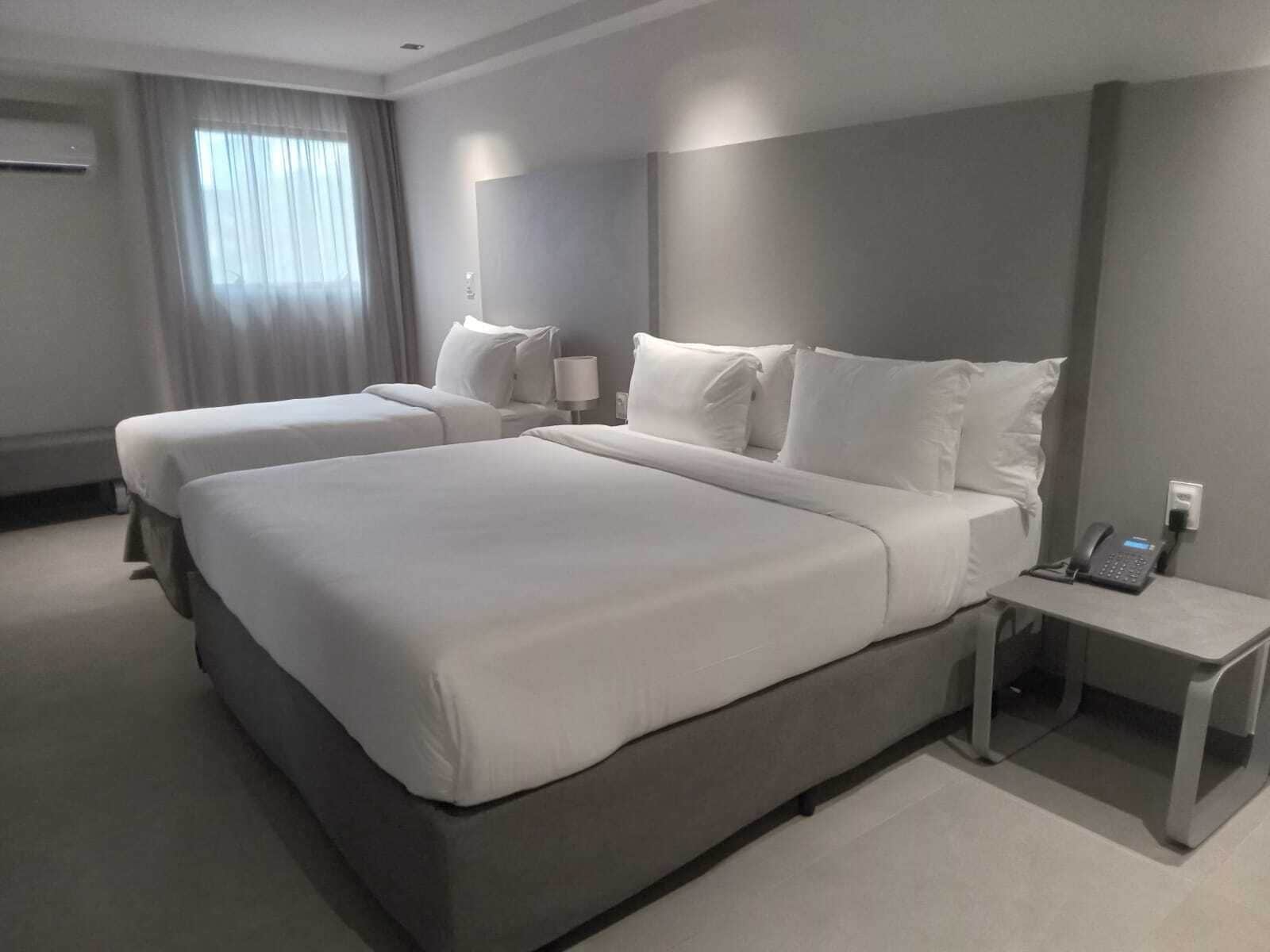 Habitación de hotel con dos camas, una mesita de noche con teléfono y una ventana con cortinas.
