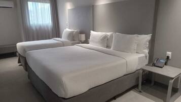 Habitación de hotel con dos camas, una mesita de noche con teléfono y una ventana con cortinas.