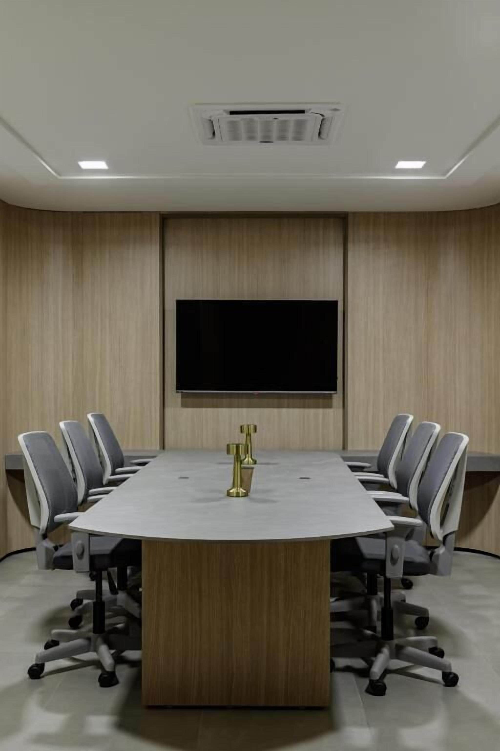 A conference room with a large table, six chairs, a flat-screen TV, and a ceiling vent.