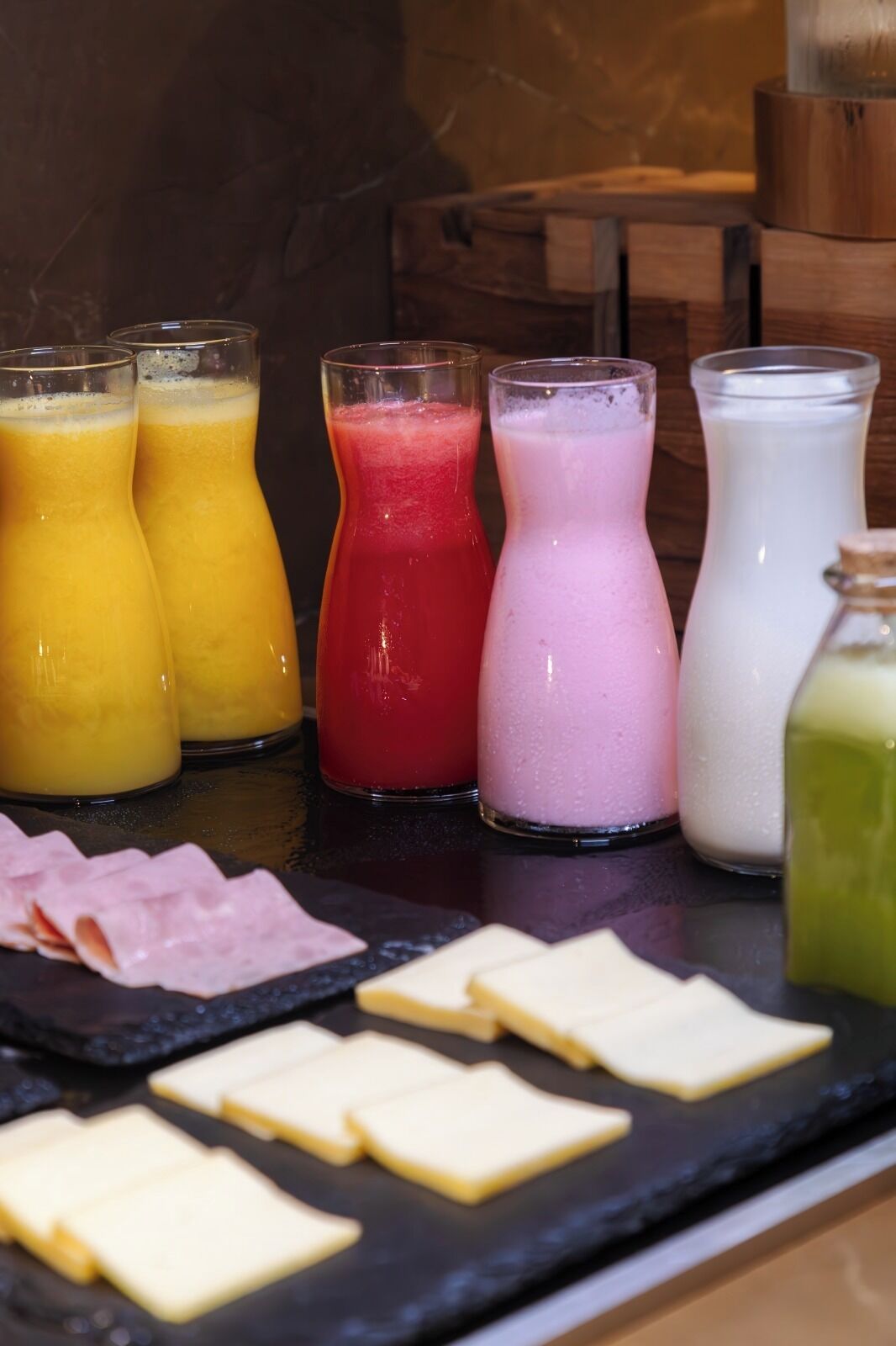 Buffet de café da manhã com diversos sucos, seleção de queijos e frios.
