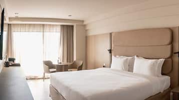 Habitación de hotel con una cama grande, un escritorio, dos sillas, un televisor montado en la pared y una ventana con cortinas.