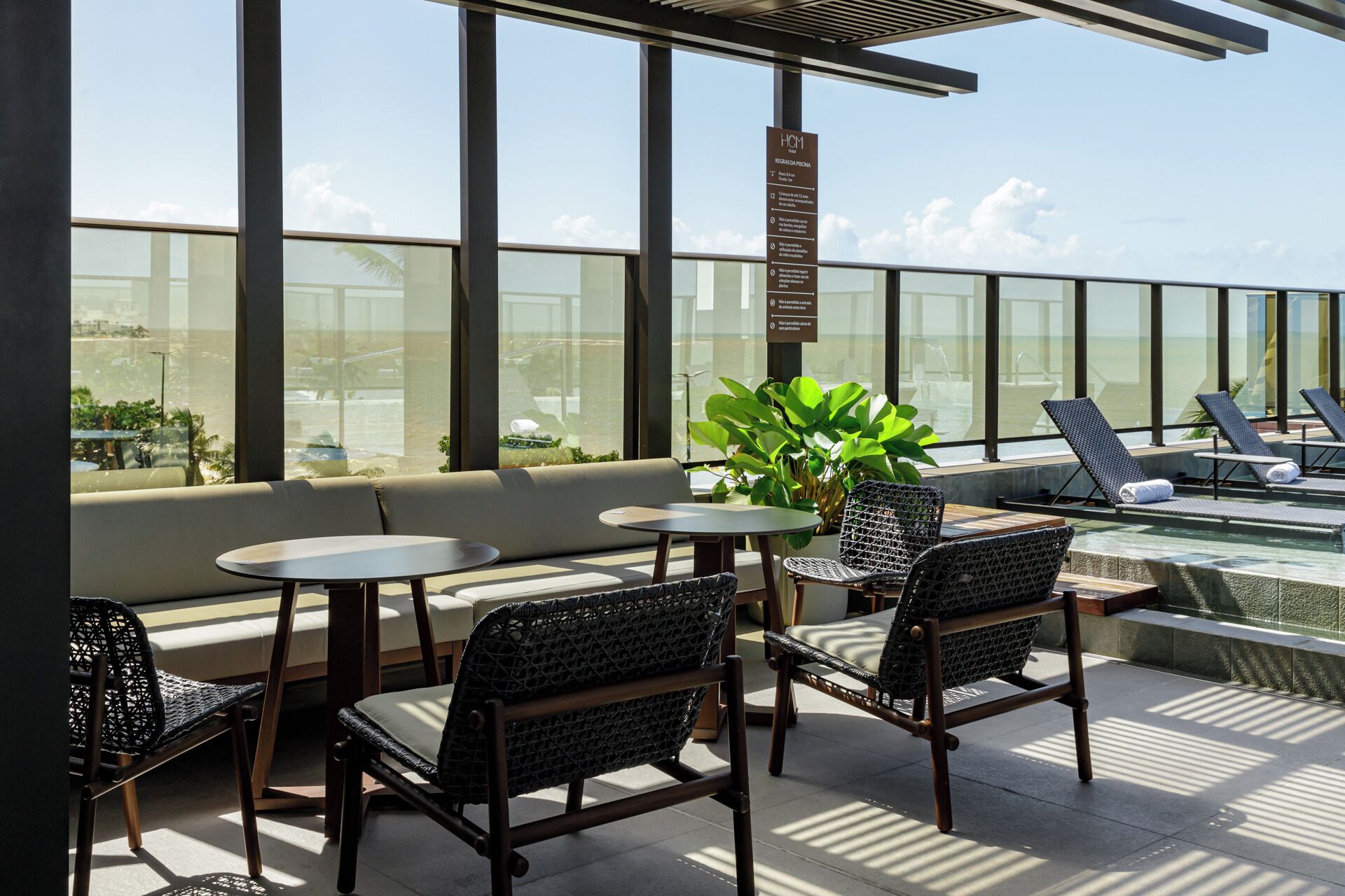 A rooftop lounge with seating, a pool, and a view of the ocean.
