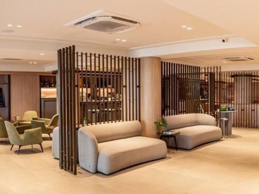 Un vestíbulo moderno de hotel con zonas de estar, un mostrador de recepción y una pantalla de televisión.