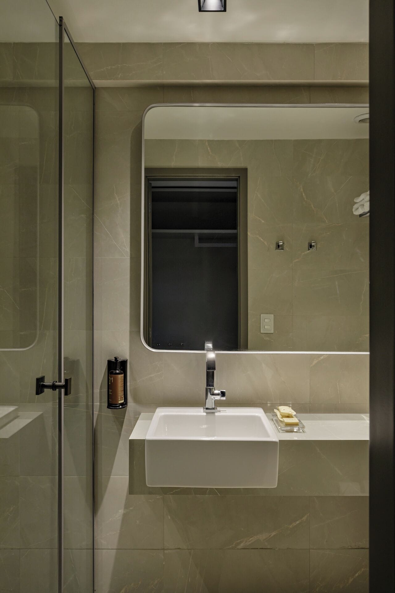 Un baño moderno con cabina de ducha de vidrio, un lavamanos blanco con espejo y una pequeña botella de jabón en la encimera.